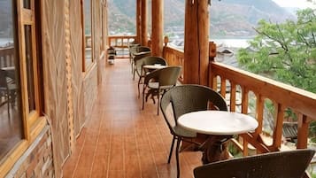 A terrace with wicker chairs and tables, overlooking a mountainous landscape.
