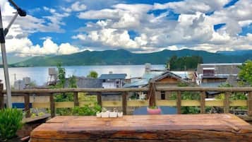 A wooden table with chairs, a view of a lake, and traditional buildings in the background.