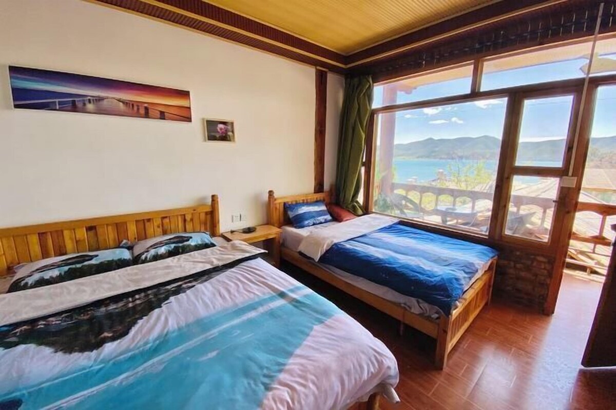 A room with two beds, a painting on the wall, and a view of mountains through large windows.