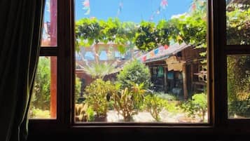 Una ventana con vista a un patio, que incluye una estructura de madera y varias plantas.