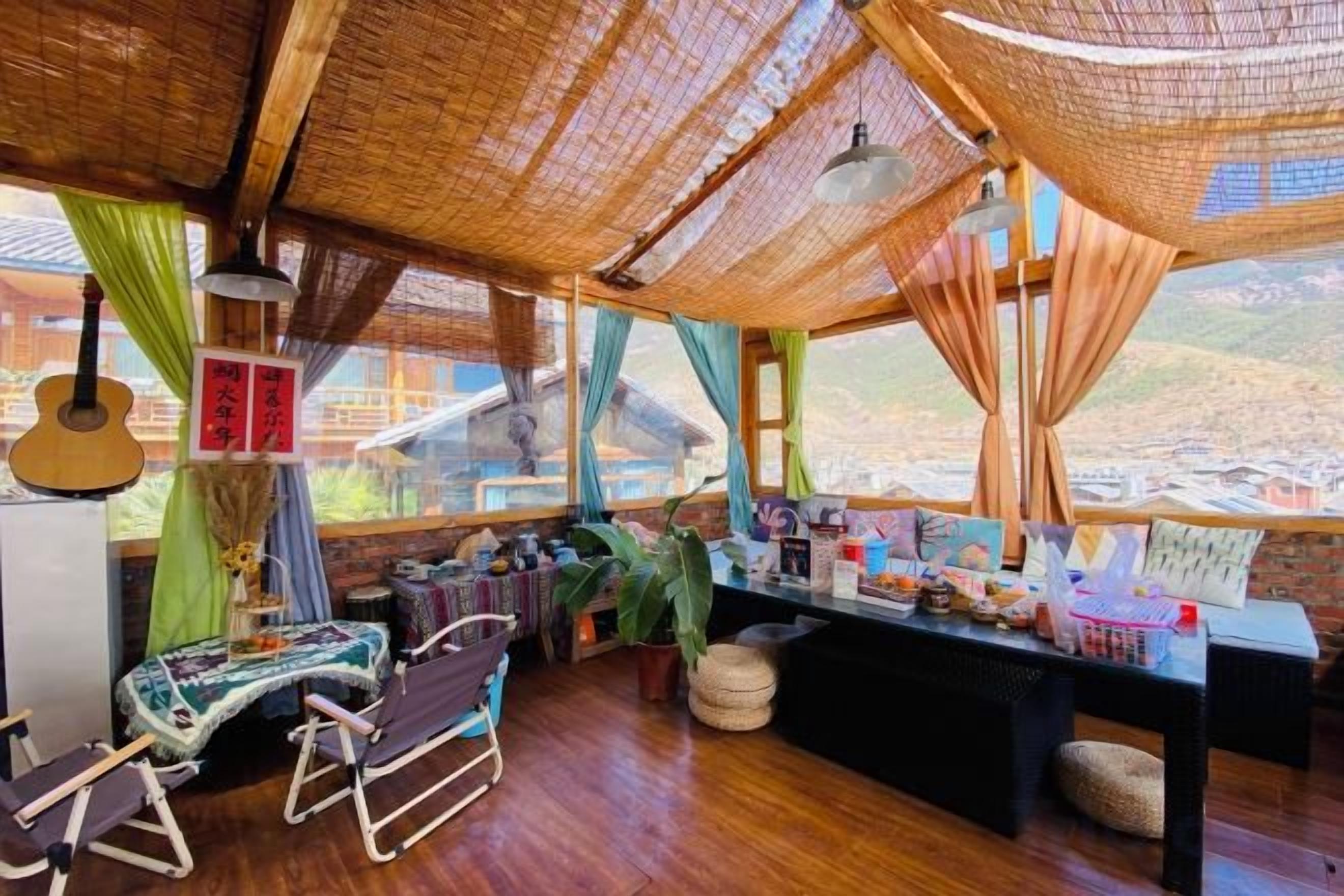 A room with a wooden floor, a dining table, chairs, a hanging guitar, and a view of a mountainous landscape through large windows.