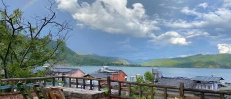 A patio with a table and chairs, overlooking a lake with buildings and mountains in the distance.