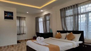 A hotel room with a large bed, a bedside table, a nightstand, a mirror, and a window with curtains. - Seven Malai Residency (Devikolam)