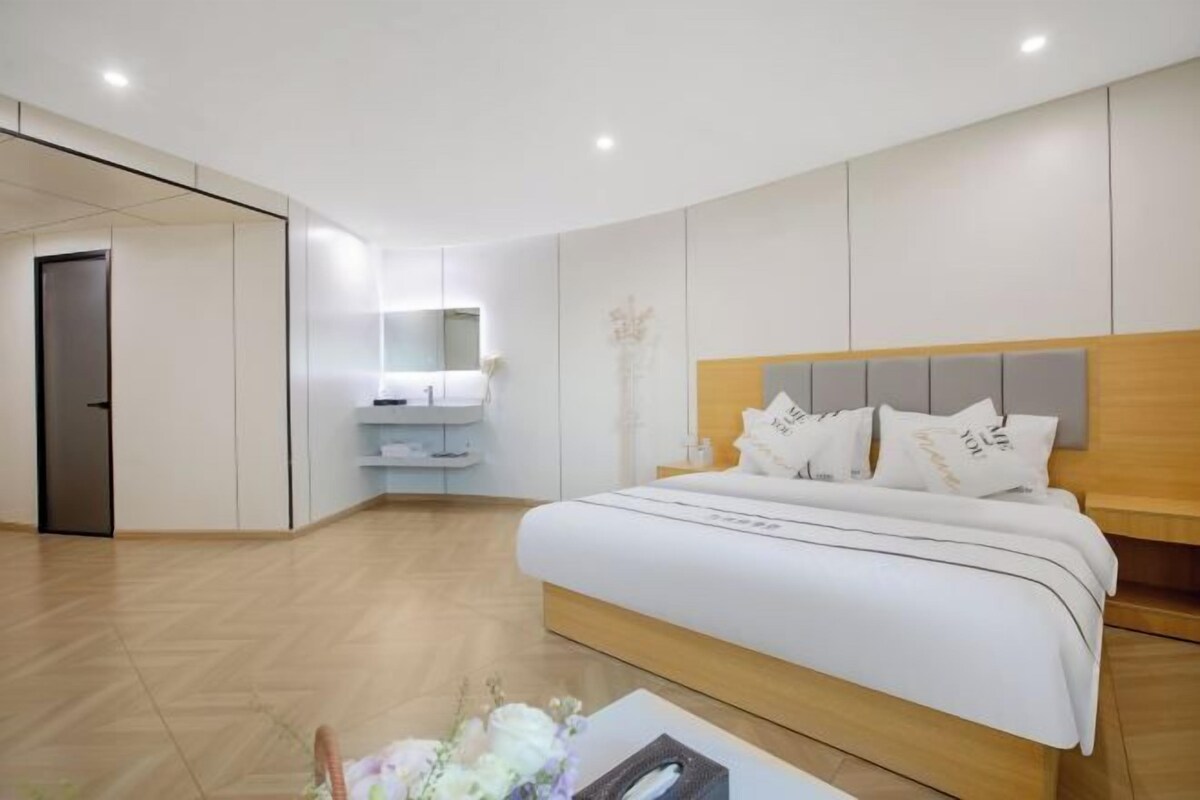 Una habitación de hotel moderna con una cama grande, una mesita de noche, un espejo y un armario empotrado.