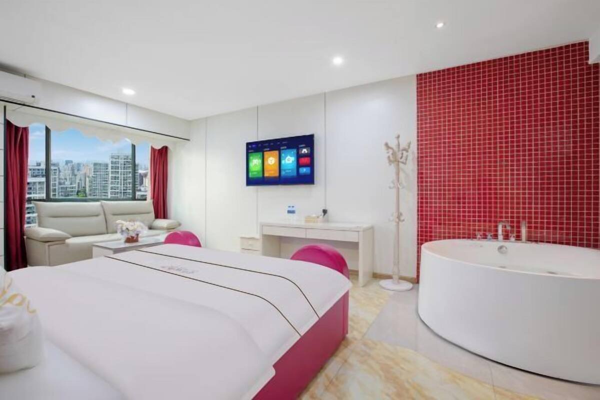 Een moderne hotelkamer met een bed, een bureau, een groot raam met uitzicht over de stad, een rode betegelde muur en een groot bad.