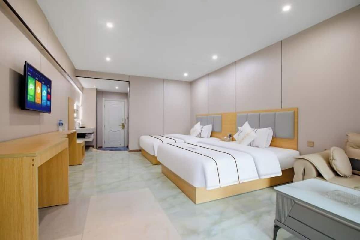 Een hotelkamer met een groot bed, een bureau, een aan de muur bevestigde televisie en een deur die naar een andere kamer leidt.