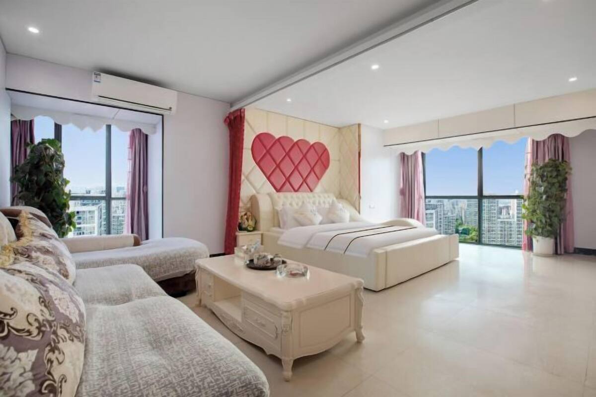 Een moderne slaapkamer met een groot bed, twee sofa's, een salontafel en een decoratieve hartvormige wand.