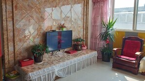 A living room with a television on a marble wall, a bench with potted plants, a red chair, and a window with curtains.