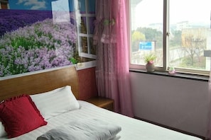 Quarto de hotel com cama, janela com vista para edifícios, uma mesinha e cortina.