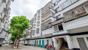 A multi-story residential building with balconies, a tree-lined street, and a parked motorcycle.