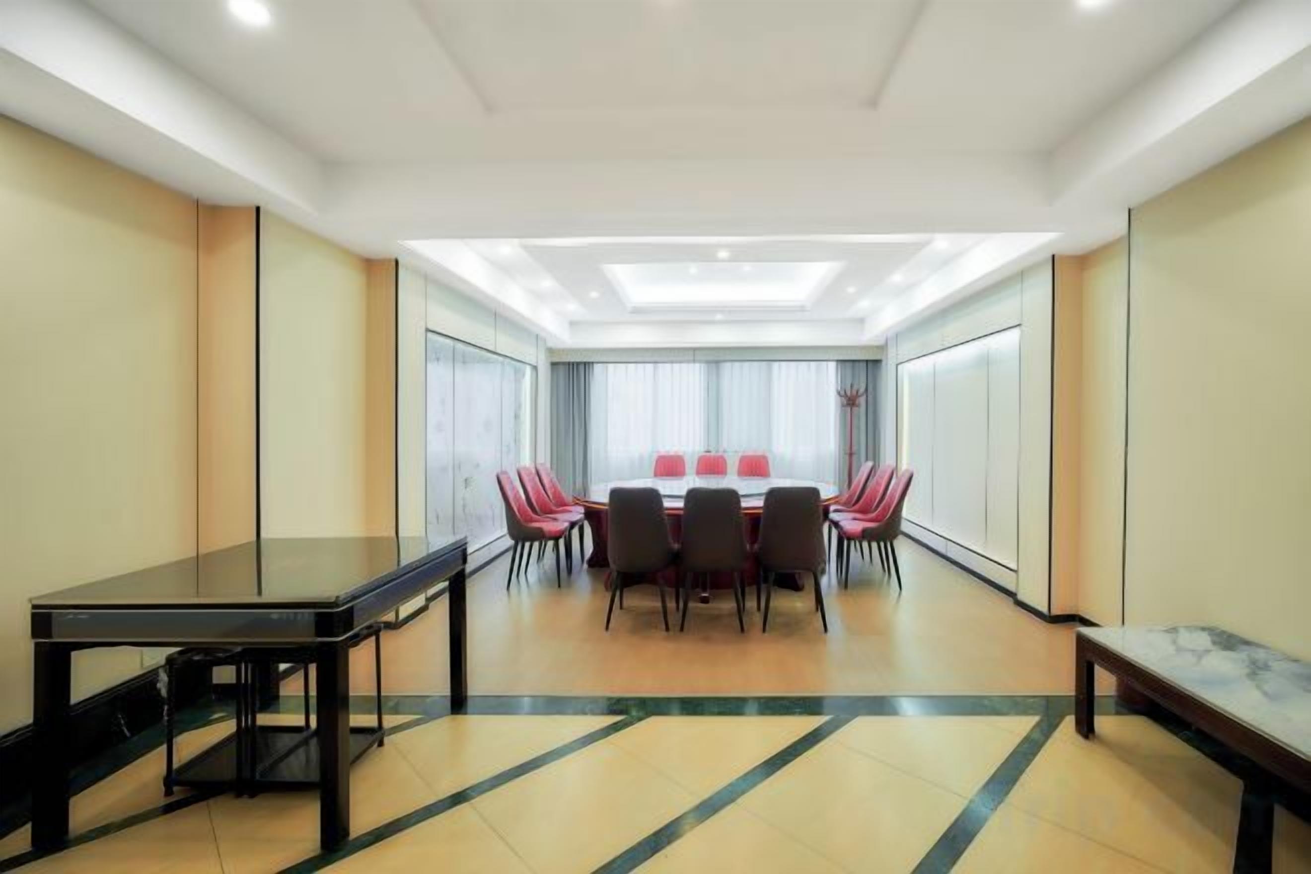 A conference room with a rectangular table, red chairs, and a long bench.