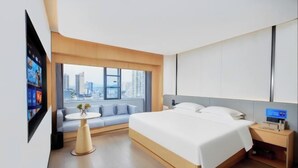A modern hotel room with a large bed, a sofa, a TV, and a city view.