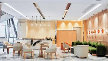 A modern hotel lobby with marble flooring, a reception desk, seating area, and a wall with lockers.