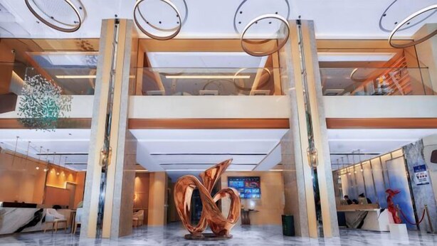 A modern hotel lobby with a marble floor, a central abstract sculpture, and a reception desk.