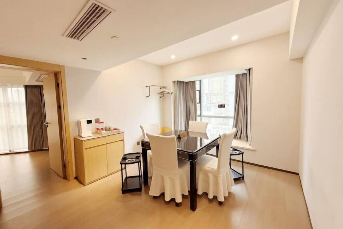 A modern hotel room with a dining area, a wooden cabinet, and a window with curtains.