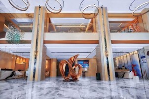 A hotel lobby with a marble floor, a reception desk, and a large abstract sculpture.