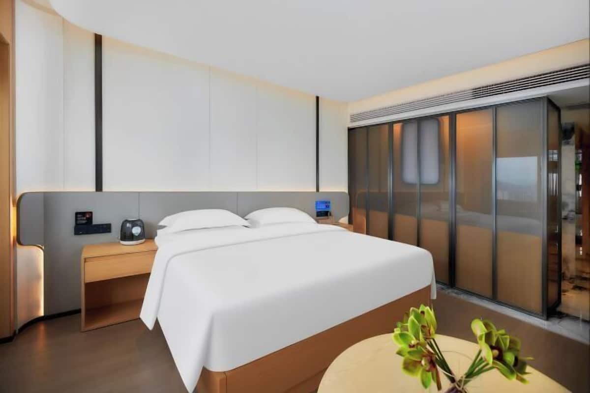 A modern hotel room with a large bed, bedside tables, a digital clock, and a sliding glass door to the outside.