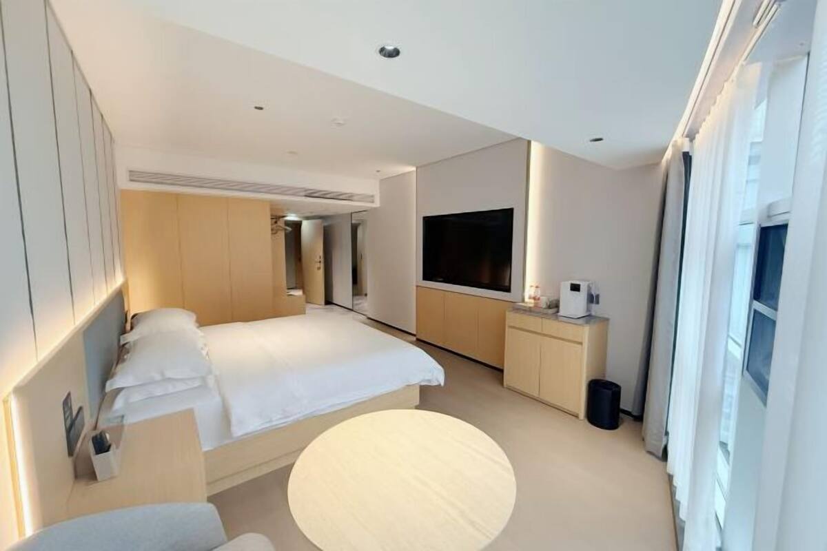 A modern hotel room with a large bed, a TV, a desk, and a round table.