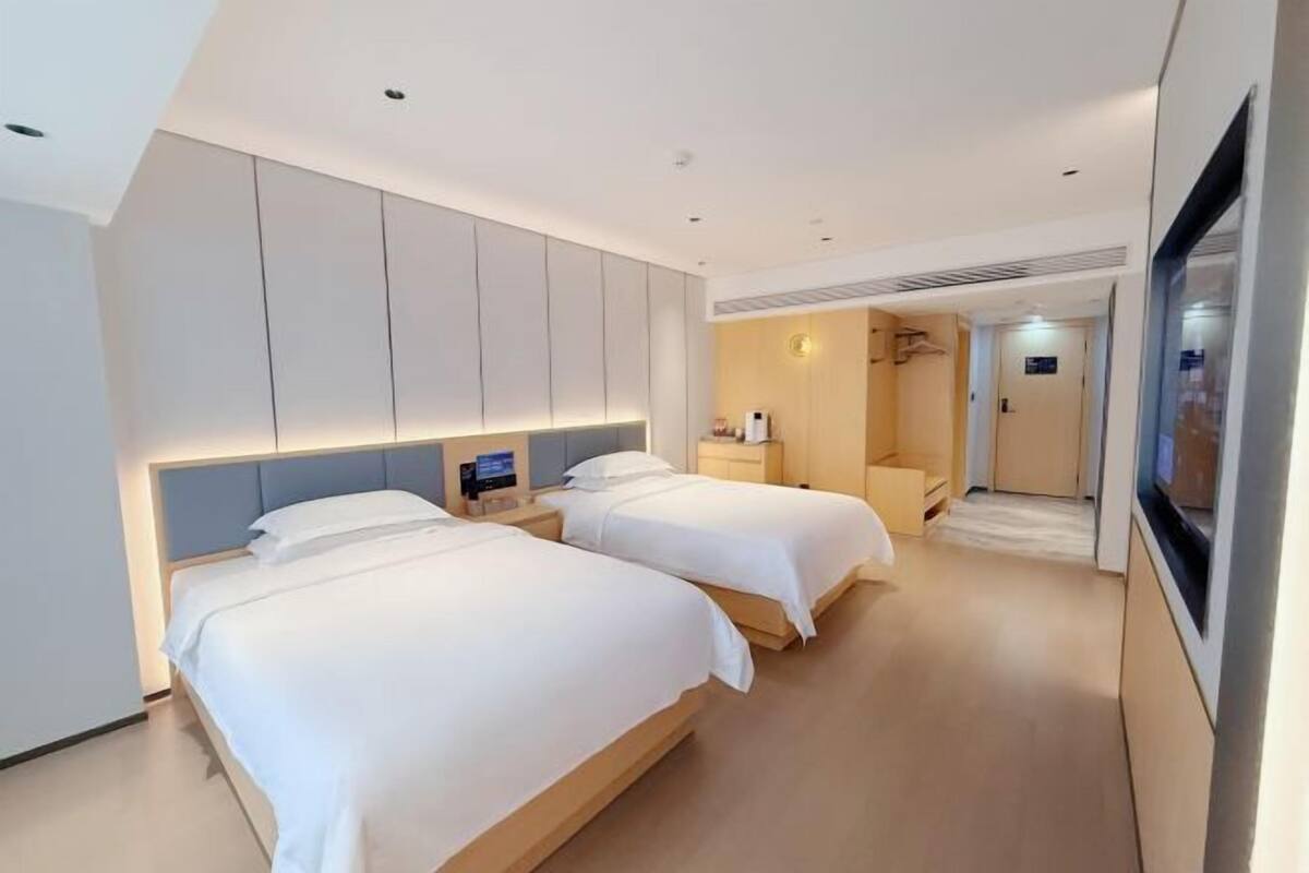 A hotel room with two beds, a TV, a minibar, and a bathroom.
