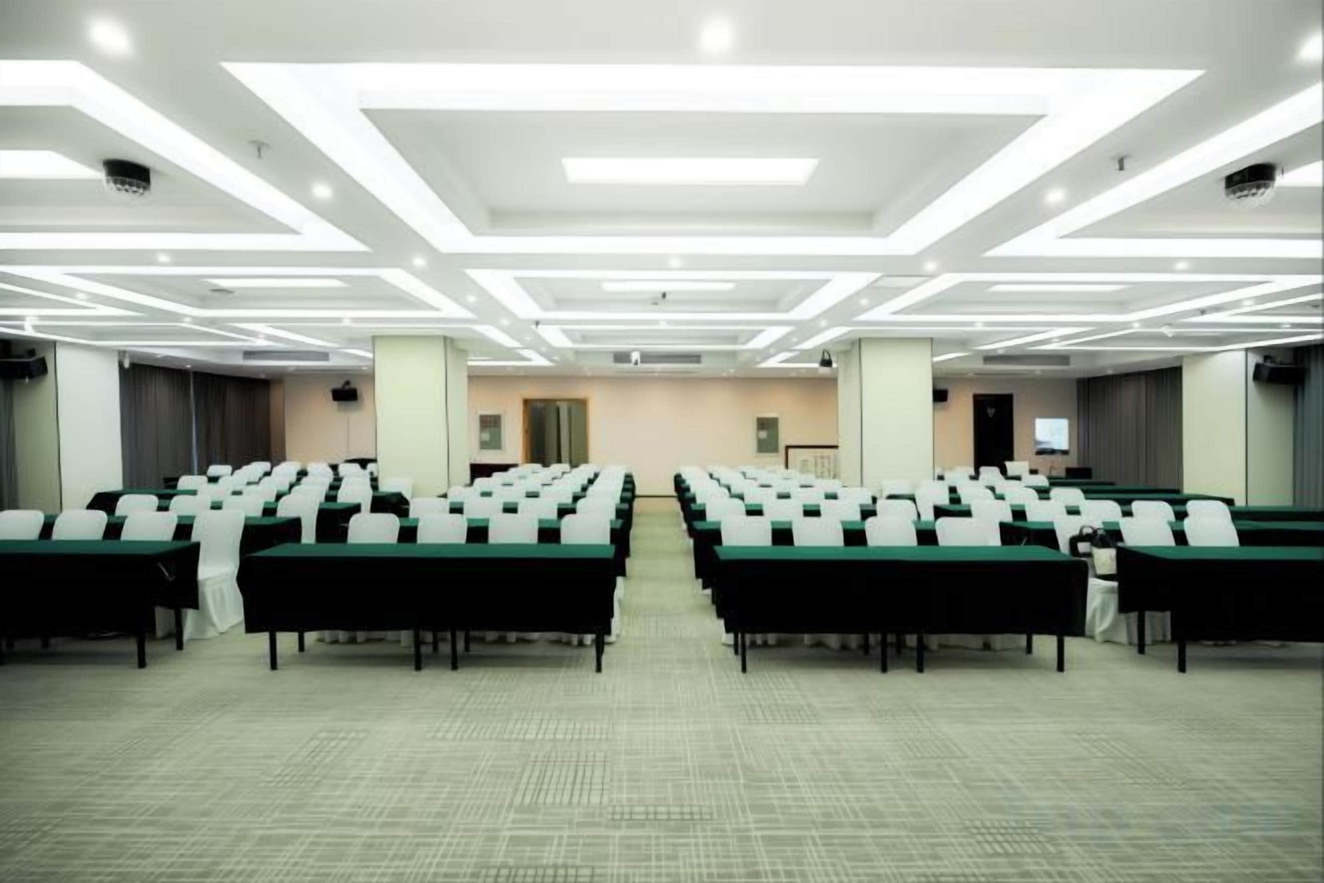 A conference room with rows of tables and chairs, a carpeted floor, and a modern ceiling design.