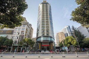 A tall, modern hotel with a curved facade, surrounded by other buildings and trees.