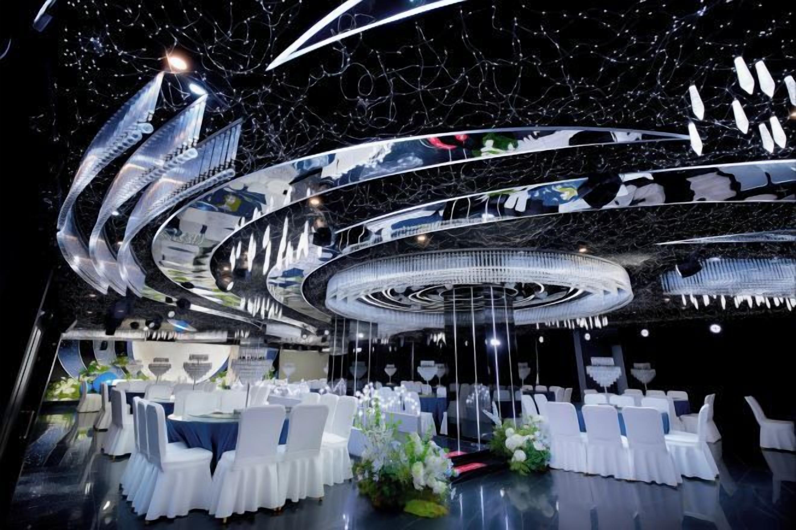 Un espace de restauration circulaire, avec des chaises et des tables blanches, un élément décoratif central et un plafond doté de surfaces réfléchissantes.