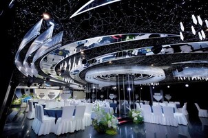A circular dining area with white chairs and tables, a central decorative element, and a ceiling with reflective surfaces.