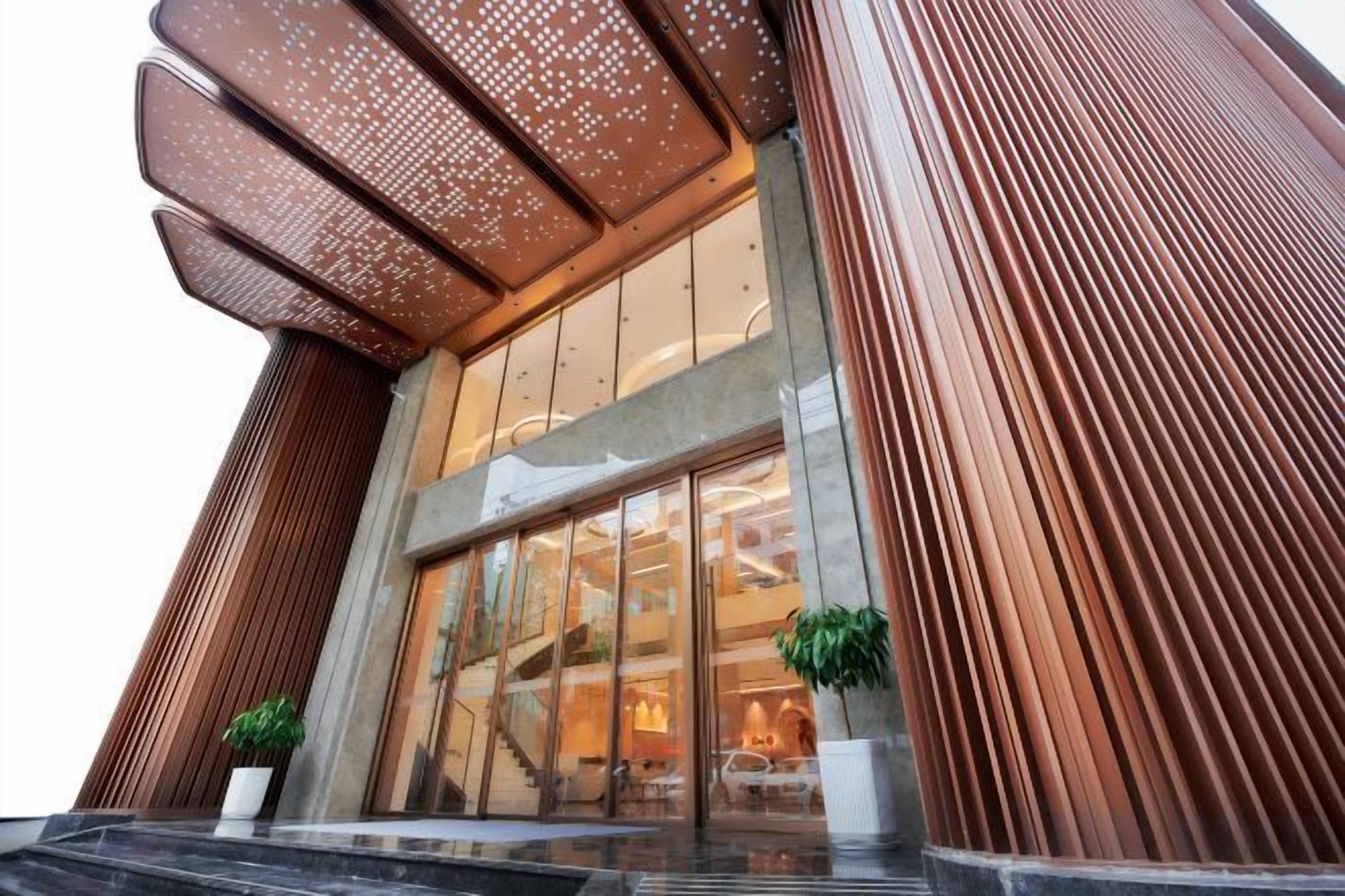A modern building with a glass facade, vertical wooden slats, and potted plants at the entrance.