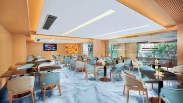 Un espace de restauration moderne, doté de plusieurs tables et chaises, d’un téléviseur à écran plat et d’un sol en marbre.