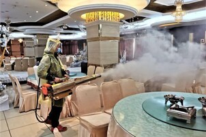 A person using a steam cleaner in a hotel room with round tables and chairs, a chandelier, and a decorative pillar.