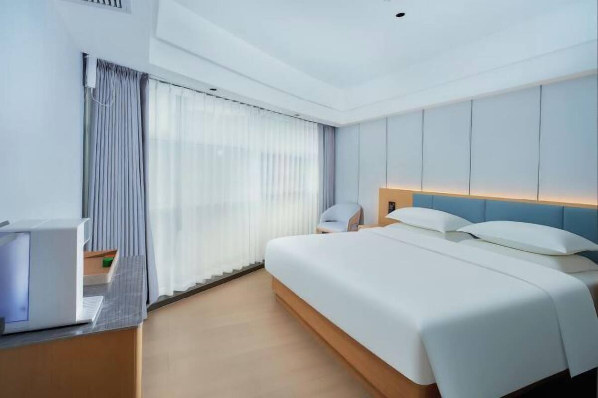A modern hotel room with a large bed, a desk with a computer, and a window with curtains.