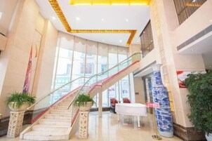 A modern hotel lobby with a glass staircase, potted plants, and a reception area.