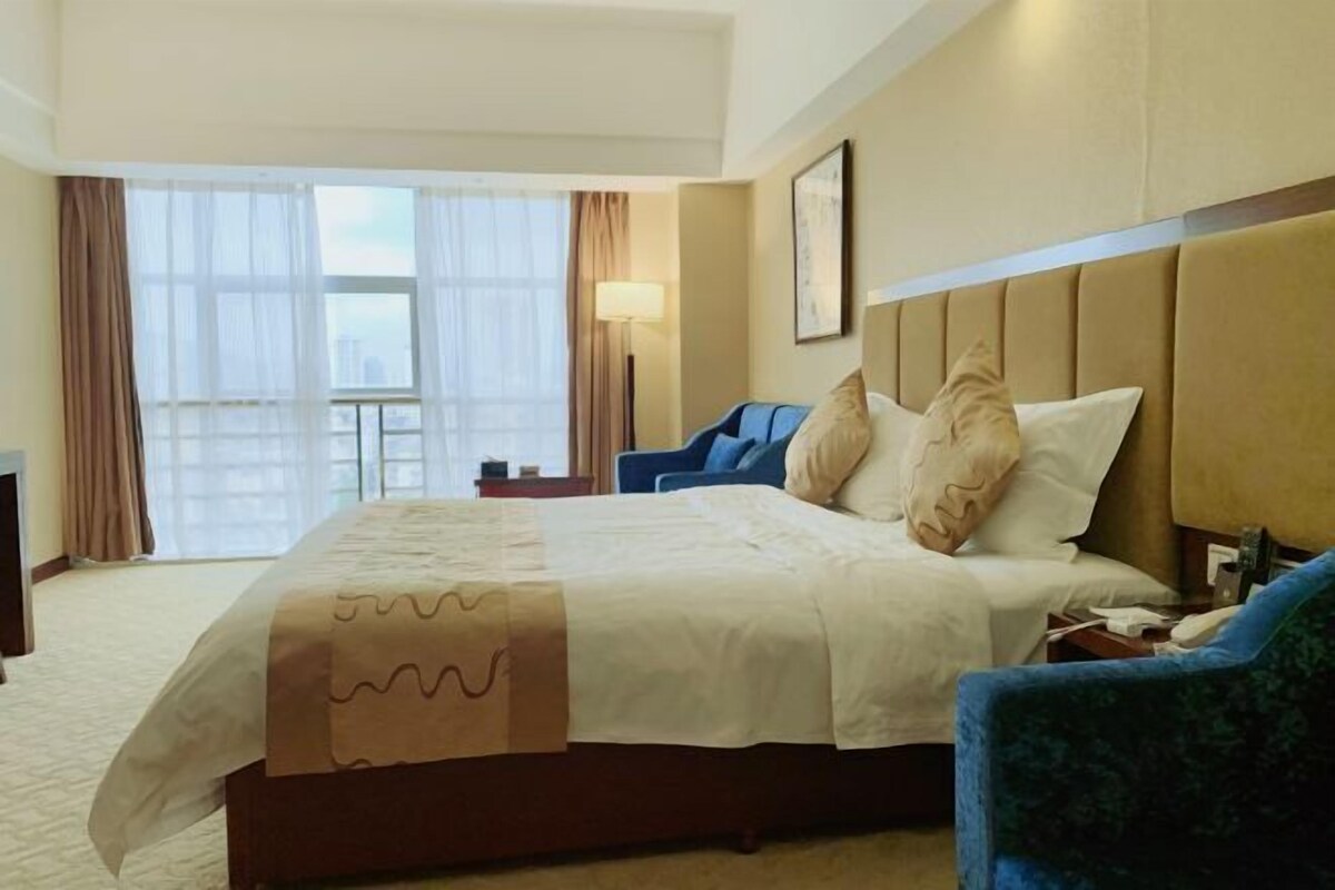 A hotel room with a large bed, a desk, a chair, and a window with curtains.