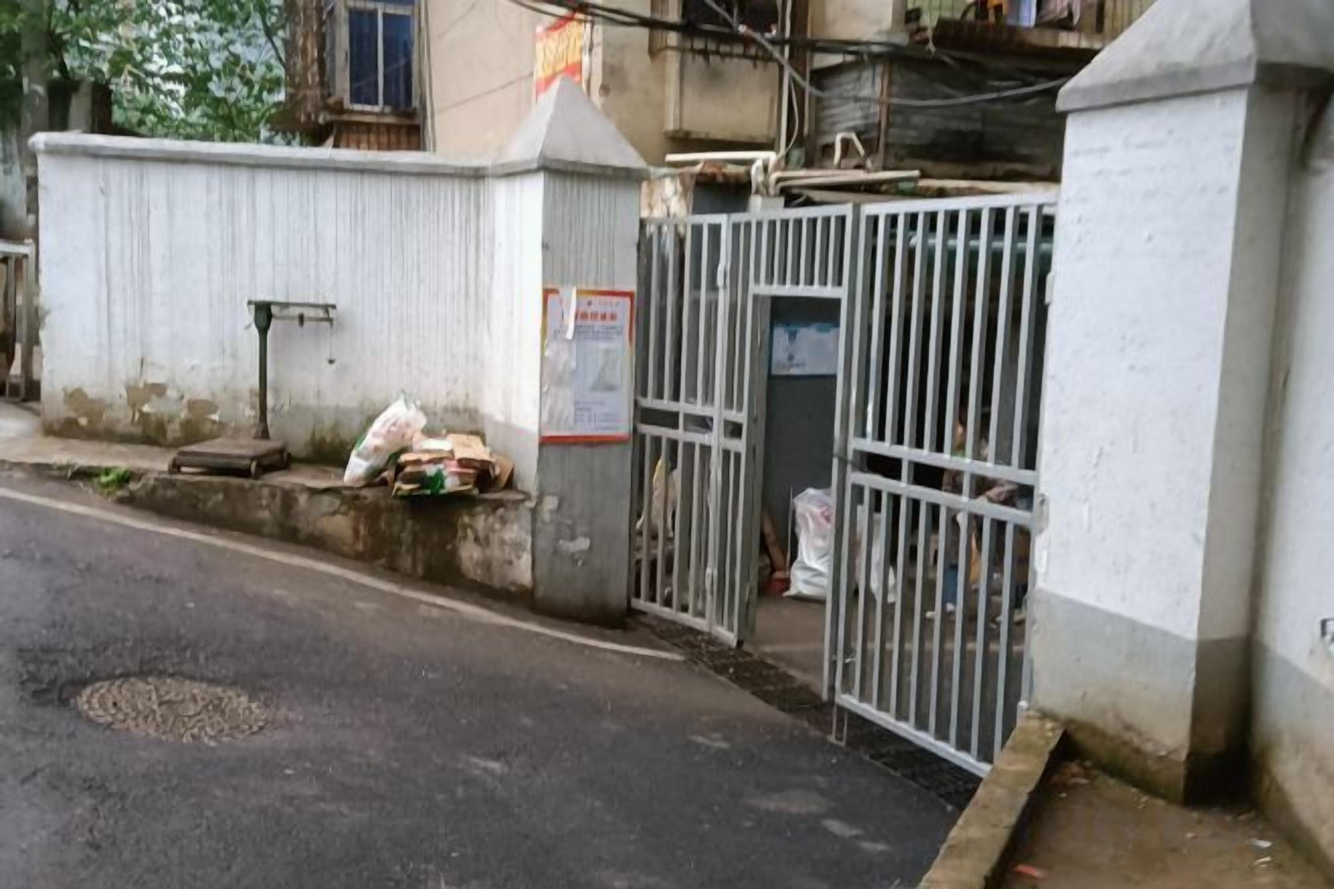 A gated entrance with a metal gate, a concrete wall, and a small step leading to a door.