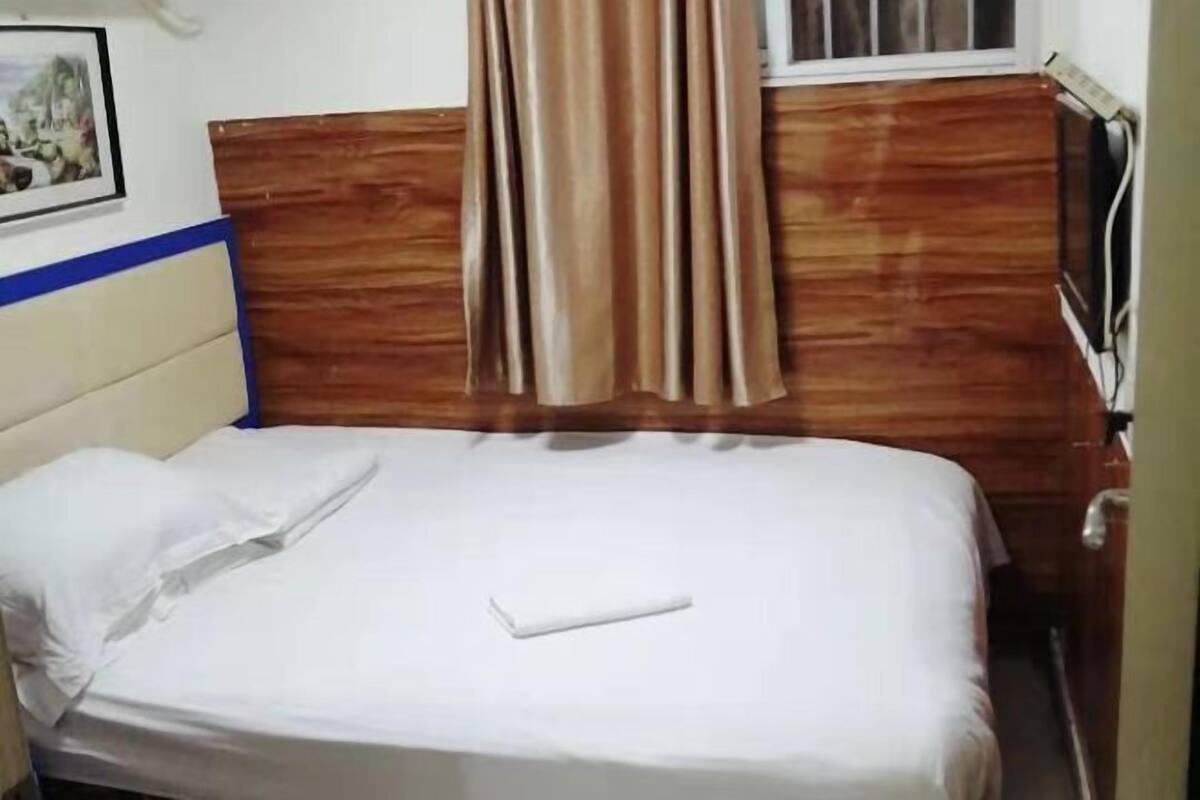 Ein Einzelbett mit Holz-Kopfteil, einem weißen Kopfkissen und einer weißen Decke.