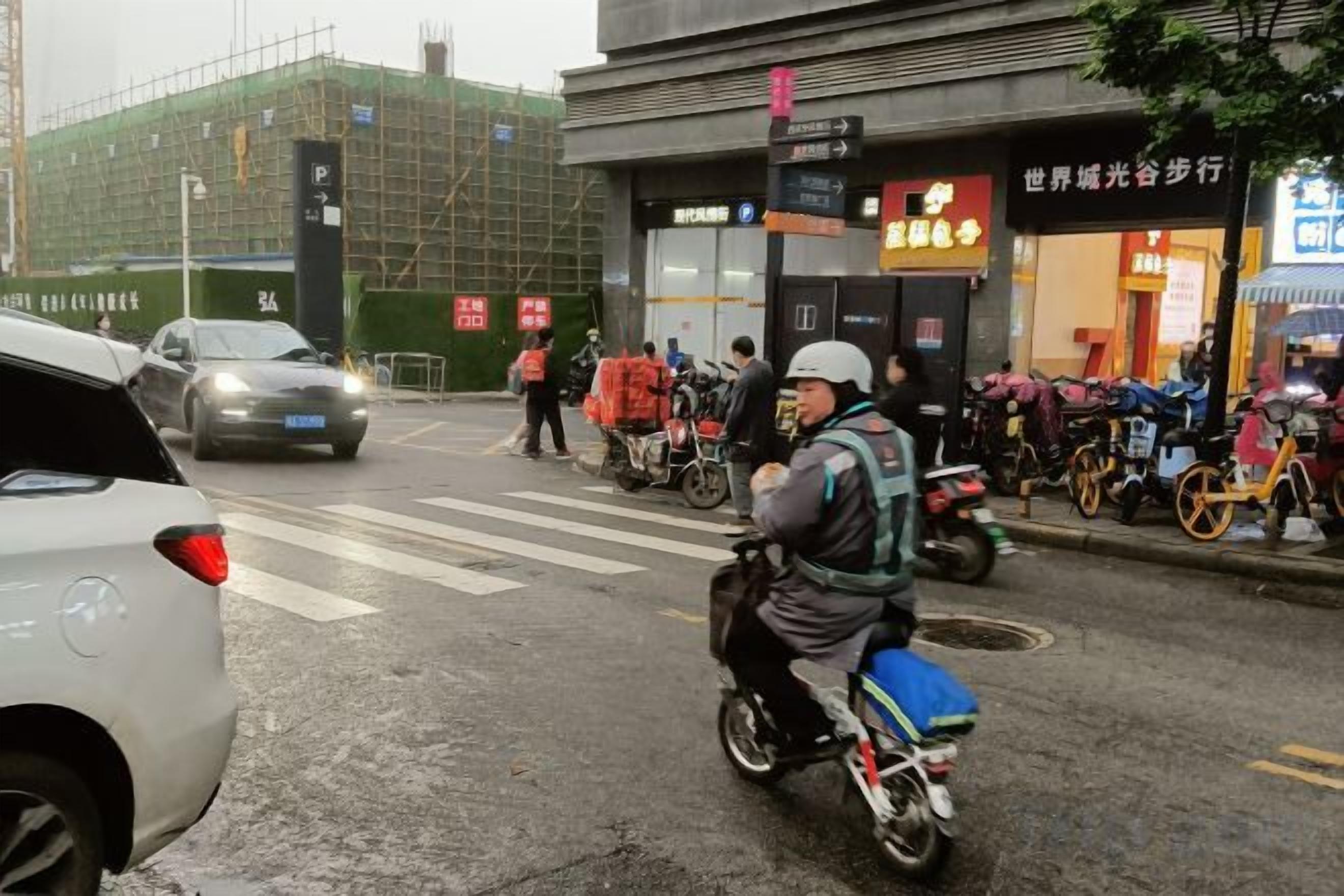 A street scene with a person on a bicycle, a car, and a building with a sign.