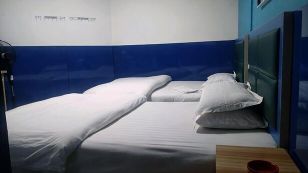 Ein Einzelbett mit weißer Bettwäsche, ein Nachttisch aus Holz mit einer roten Schale und eine Farbgestaltung in Blau und Weiß.