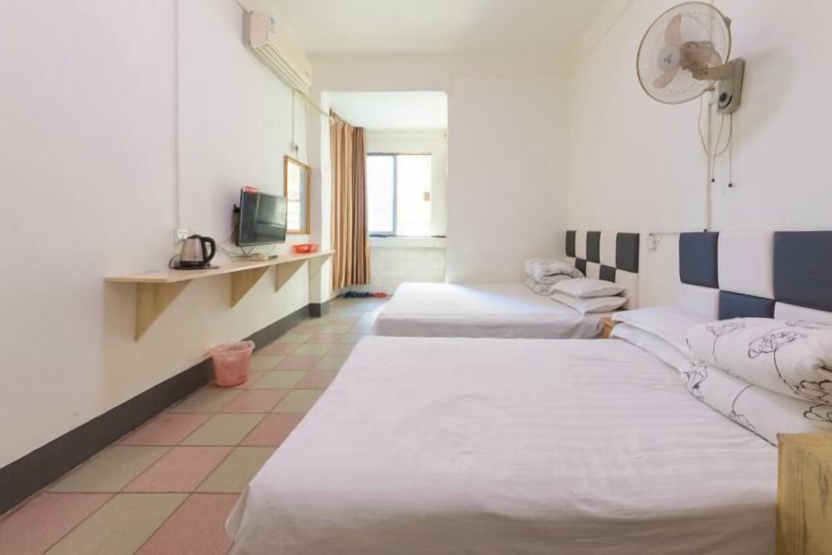 Quarto de hotel com duas camas, televisão, ventilador e uma pequena mesa com chaleira.