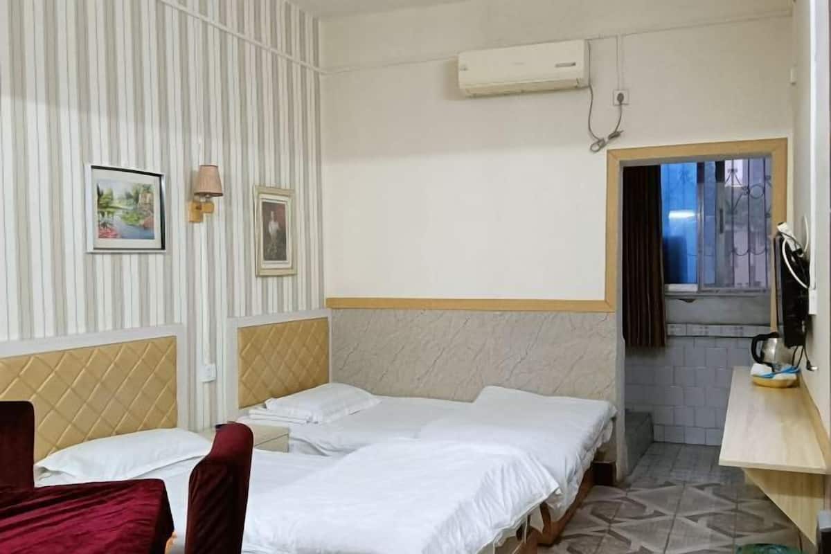 Ein Hotelzimmer mit zwei Betten, einer kleinen Küchenzeile und einem Fenster mit Vorhängen.