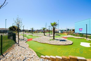 A golf course with a blue building, trees, and a clear sky.
