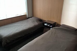 Una habitación de hotel con dos camas individuales, una mesita de noche de madera y un ventanal con cortinas.