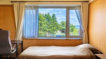 A hotel room with a bed, a chair, a desk, and a window with curtains.