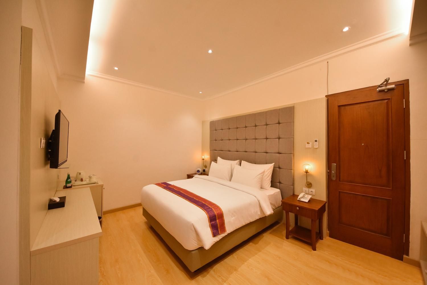 A hotel room with a bed, bedside tables, a TV, a wardrobe, and a door.