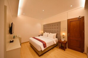 A hotel room with a bed, bedside tables, a TV, a wardrobe, and a door. - Khas Ombilin Hotel (Saringan)