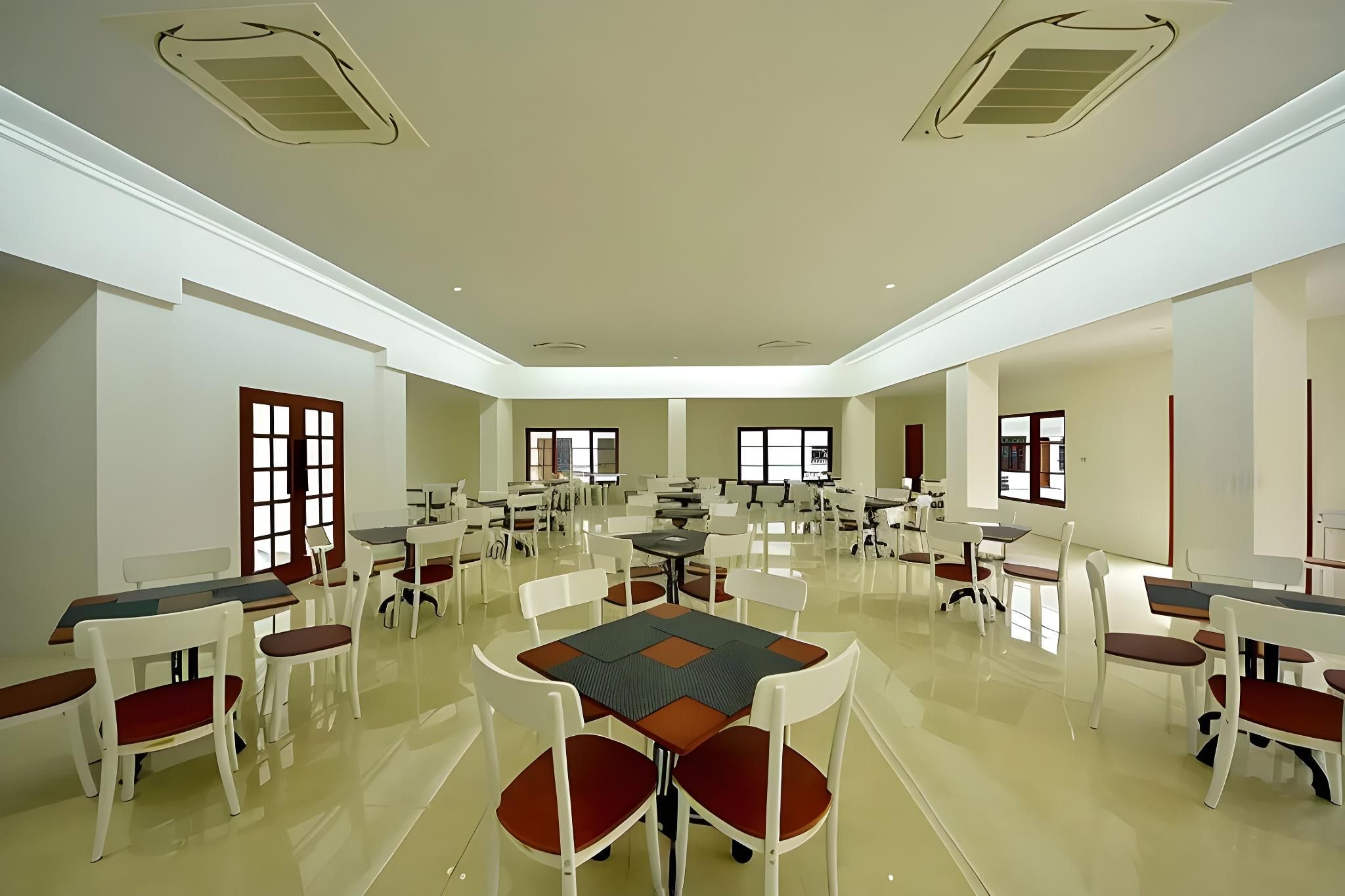 A spacious conference room with multiple tables and chairs, large windows, and a high ceiling.