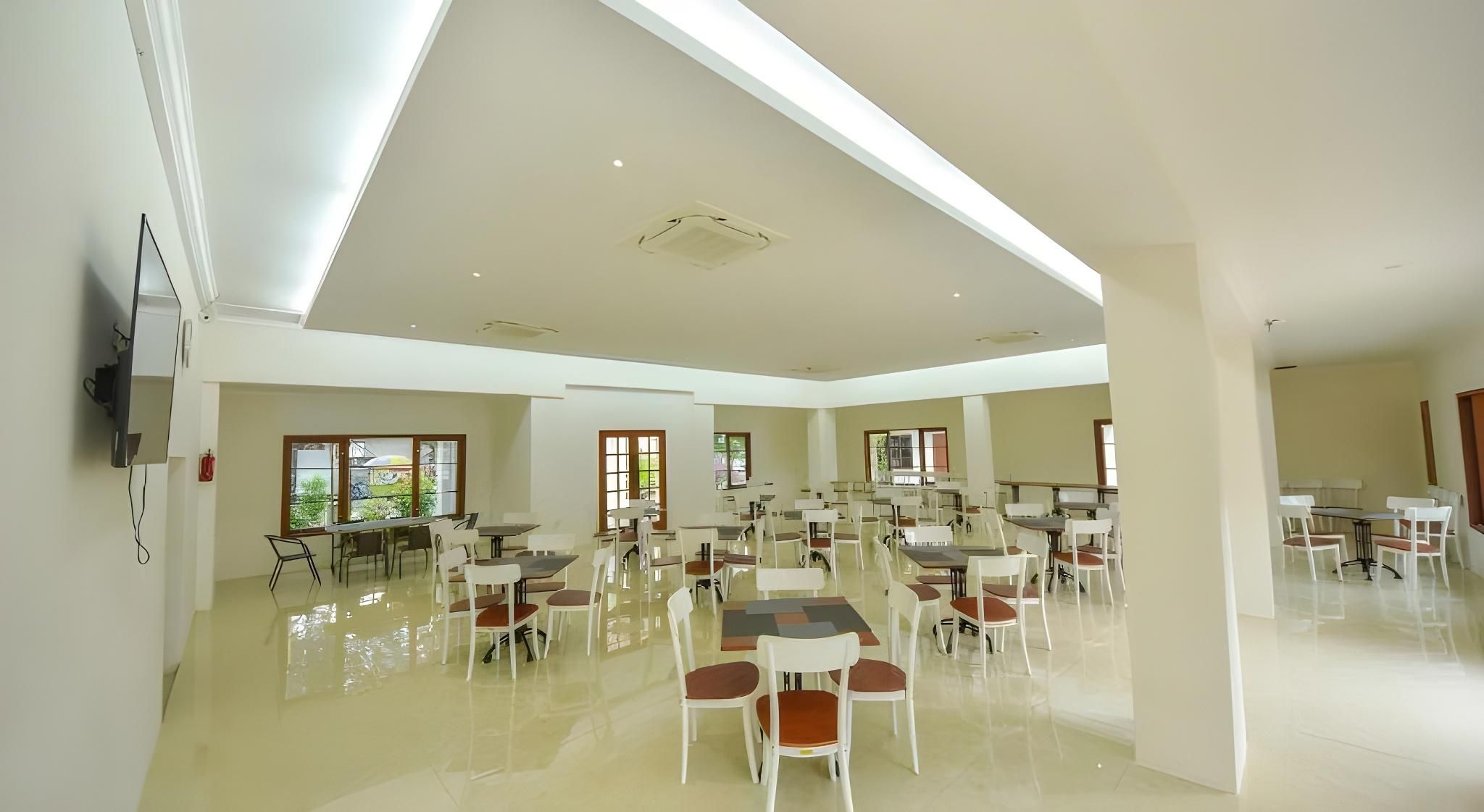 A spacious indoor area with multiple tables and chairs, large windows, and a flat ceiling with recessed lighting.