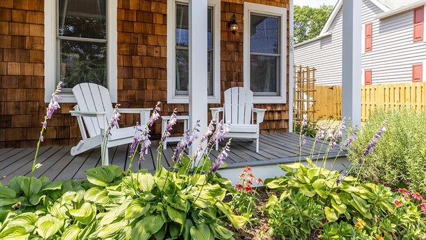 Une maison en bois avec un porche, deux fauteuils Adirondack blancs et une variété de plantes.