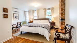 Une chambre avec un grand lit, deux chaises, une table de chevet et un mur en briques.