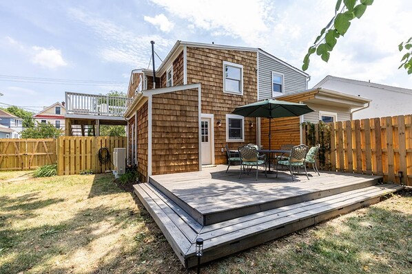 A backyard with a wooden deck, a dining table with chairs, and a covered patio area.