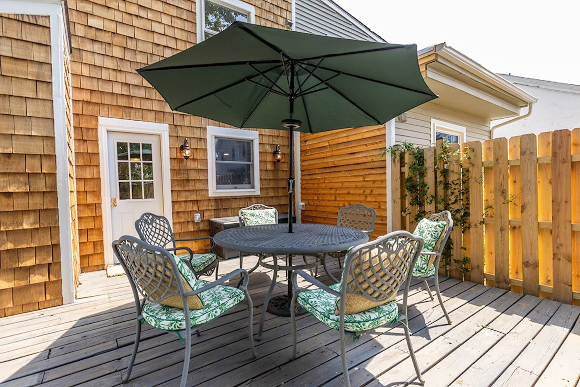 A wooden deck with a round table and four chairs, an umbrella, and a wooden fence.